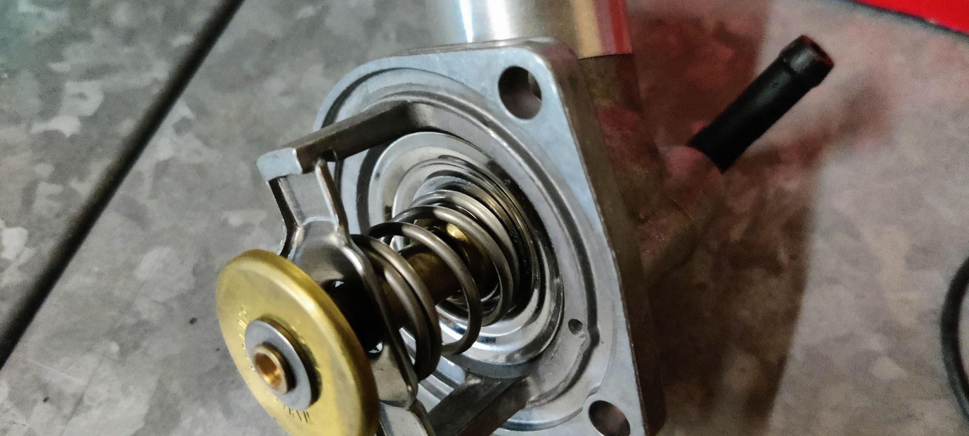 Een thermostaat van het merk Wahler, de rode en blauwe verpakking ervan, en een rubberen O-ringafdichting, tentoongesteld op een tegelvloer.