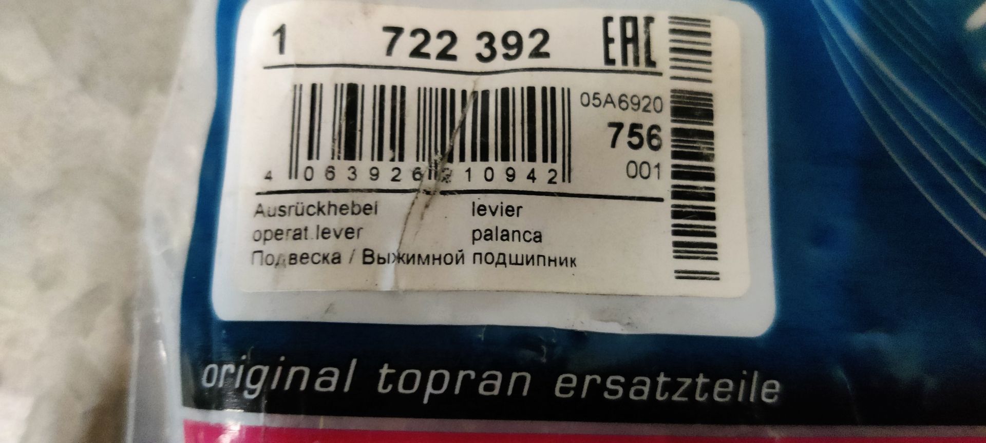 Een zwarte koppelingshendel voor auto's ligt op een tegelvloer naast de verpakking en het bubbeltjesplastic.
