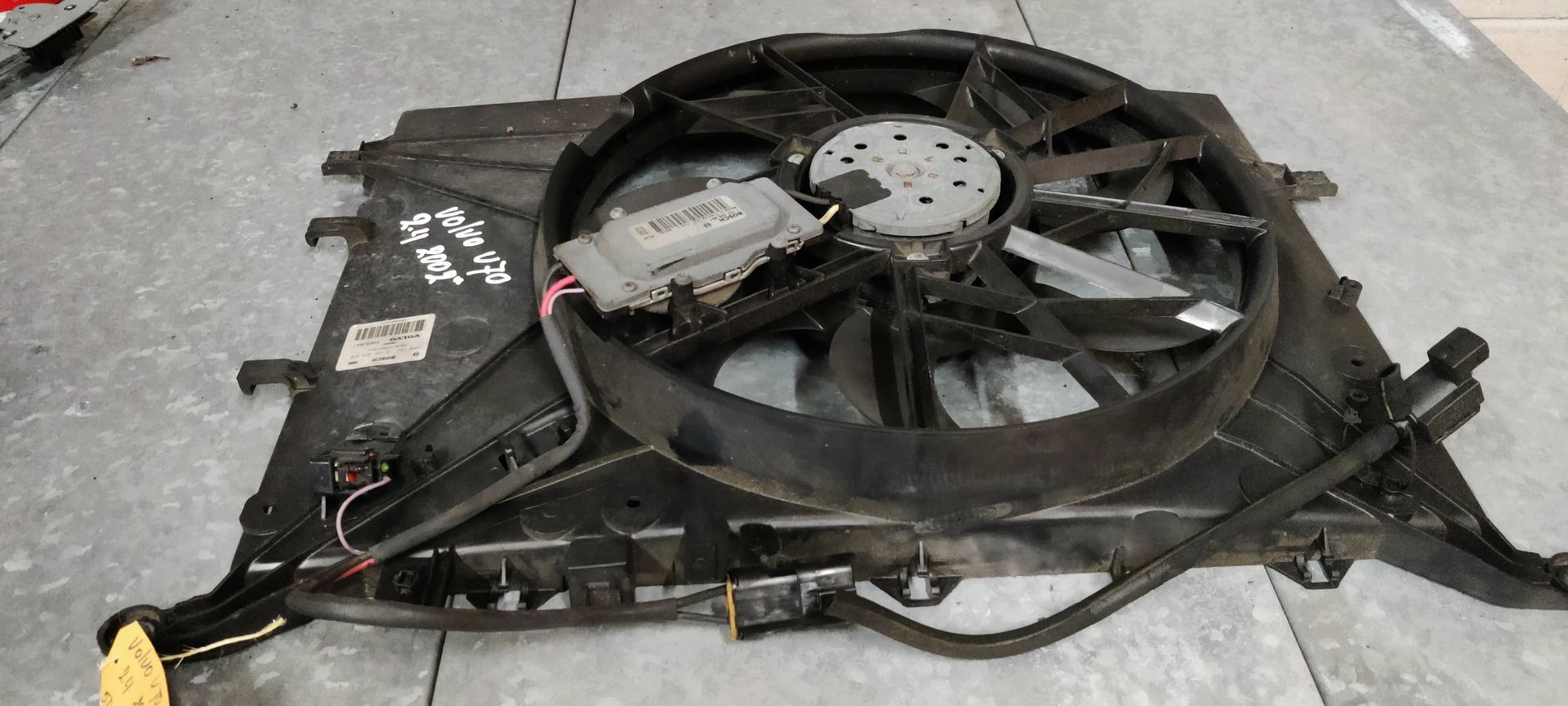 Zwarte koelventilator voor autoradiatoren met een aangehechte elektronische regelmodule op een grijze ondergrond.