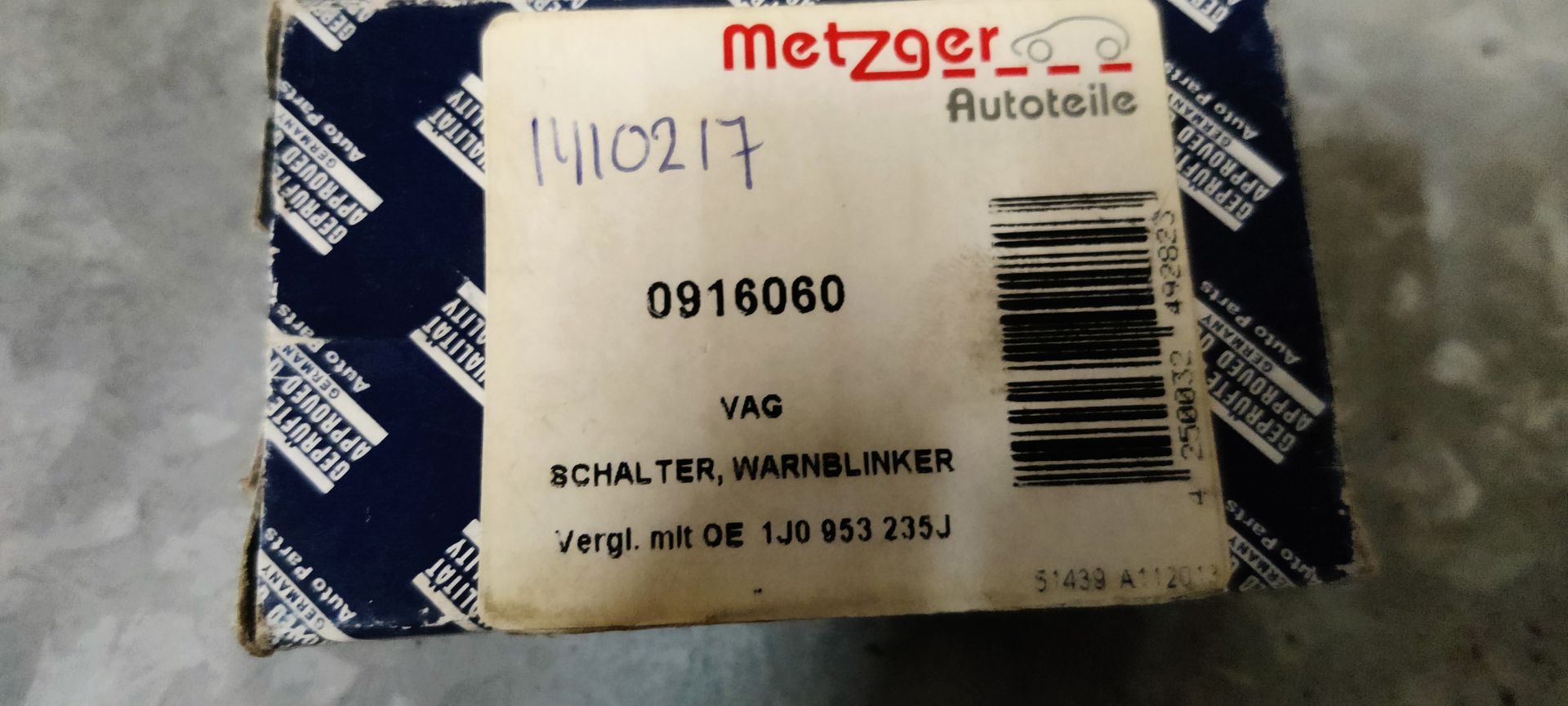Een zwarte autoalarmlichtschakelaar met een rood driehoekssymbool, die op een grijze ondergrond voor de productverpakking staat.