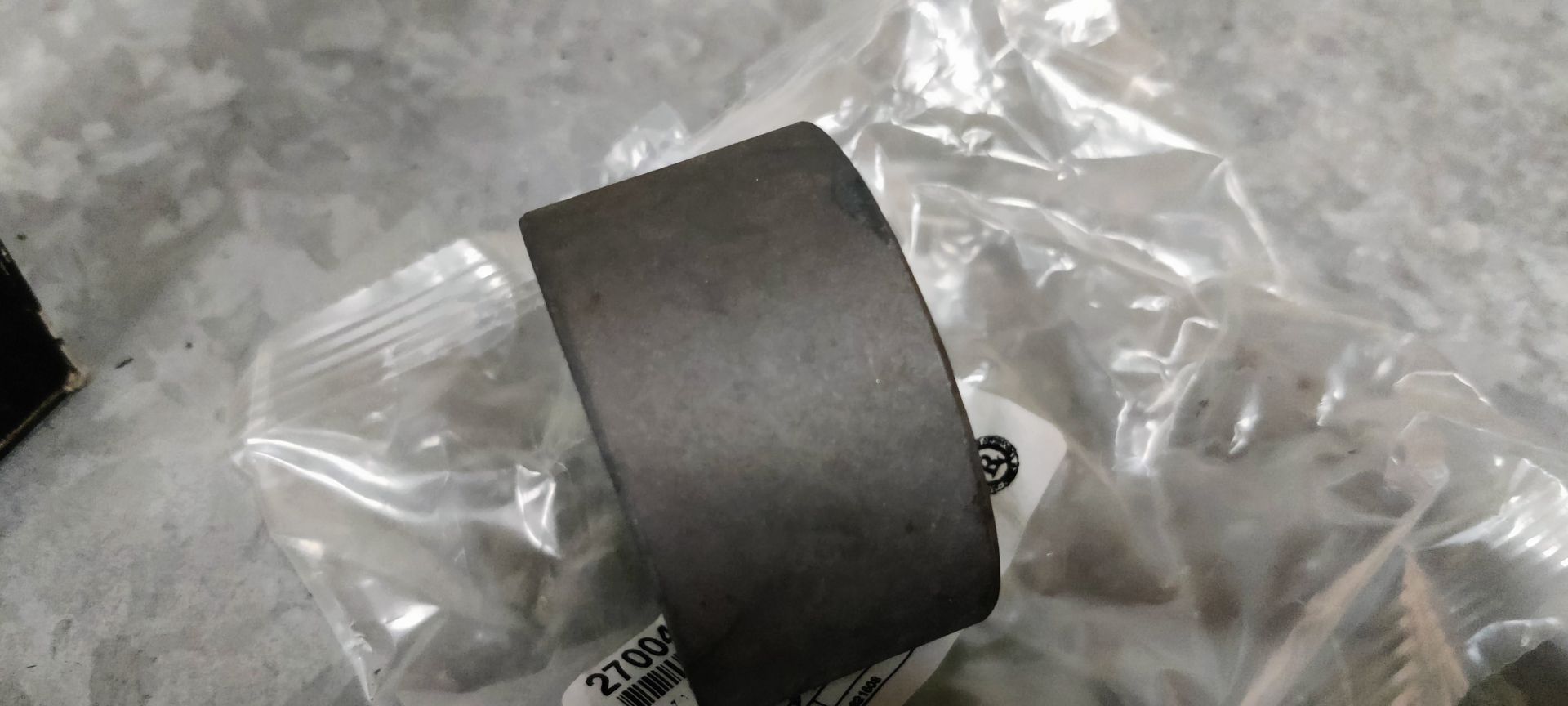 Een zwart, cilindrisch rubberen busje voor auto's, schuin geplaatst zodat het binnenste gat zichtbaar is, rustend op een transparante plastic verpakking.