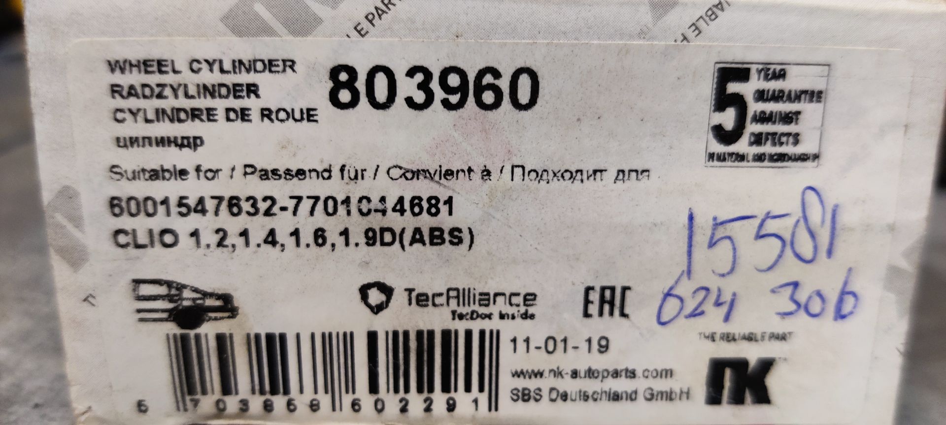 Een metalen wielcilinder voor een Renault Clio, rustend op een grijze ondergrond naast een doos met handgeschreven tekst.