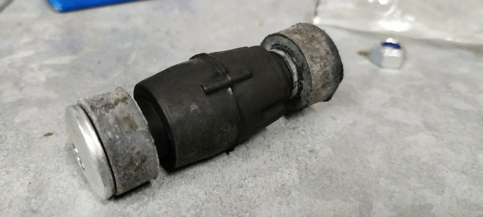 Een blauwe SKF-onderdelendoos, een plastic zak, een klein metalen moertje en een cilindrisch zwart motoronderdeel van rubber en metaal.