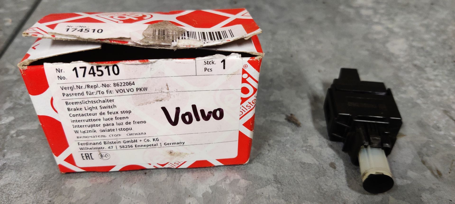 Een doos van het merk FEBI met label 174510 voor Volvo, naast een zwart-witte plastic remlichtschakelaar voor auto's.