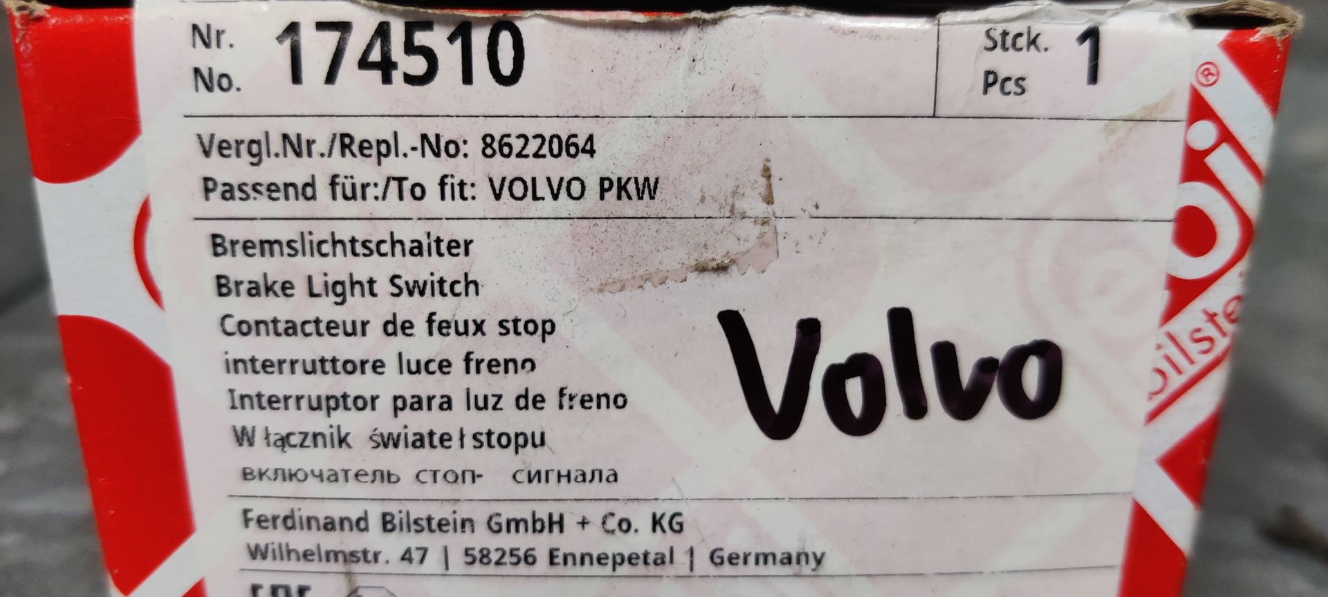 Een doos van het merk FEBI met label 174510 voor Volvo, naast een zwart-witte plastic remlichtschakelaar voor auto's.