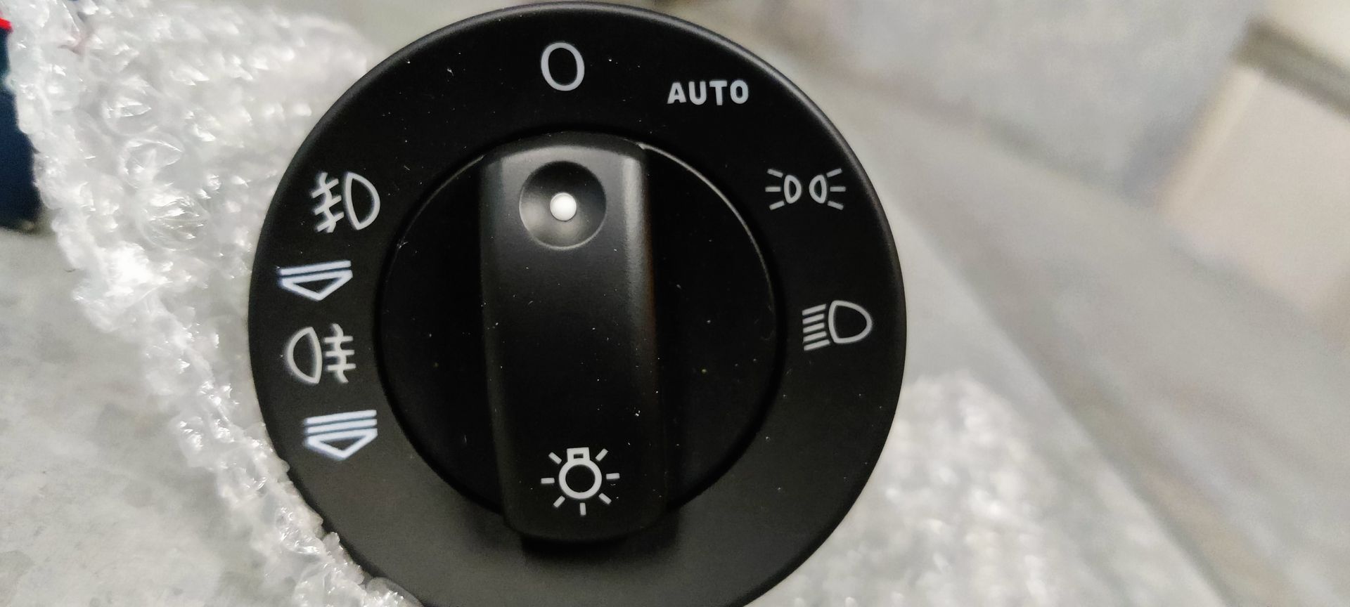 Een doosje van het merk Topran naast een zwarte bedieningsschakelaar voor autokoplampen, geplaatst op een lichtgekleurde ondergrond.