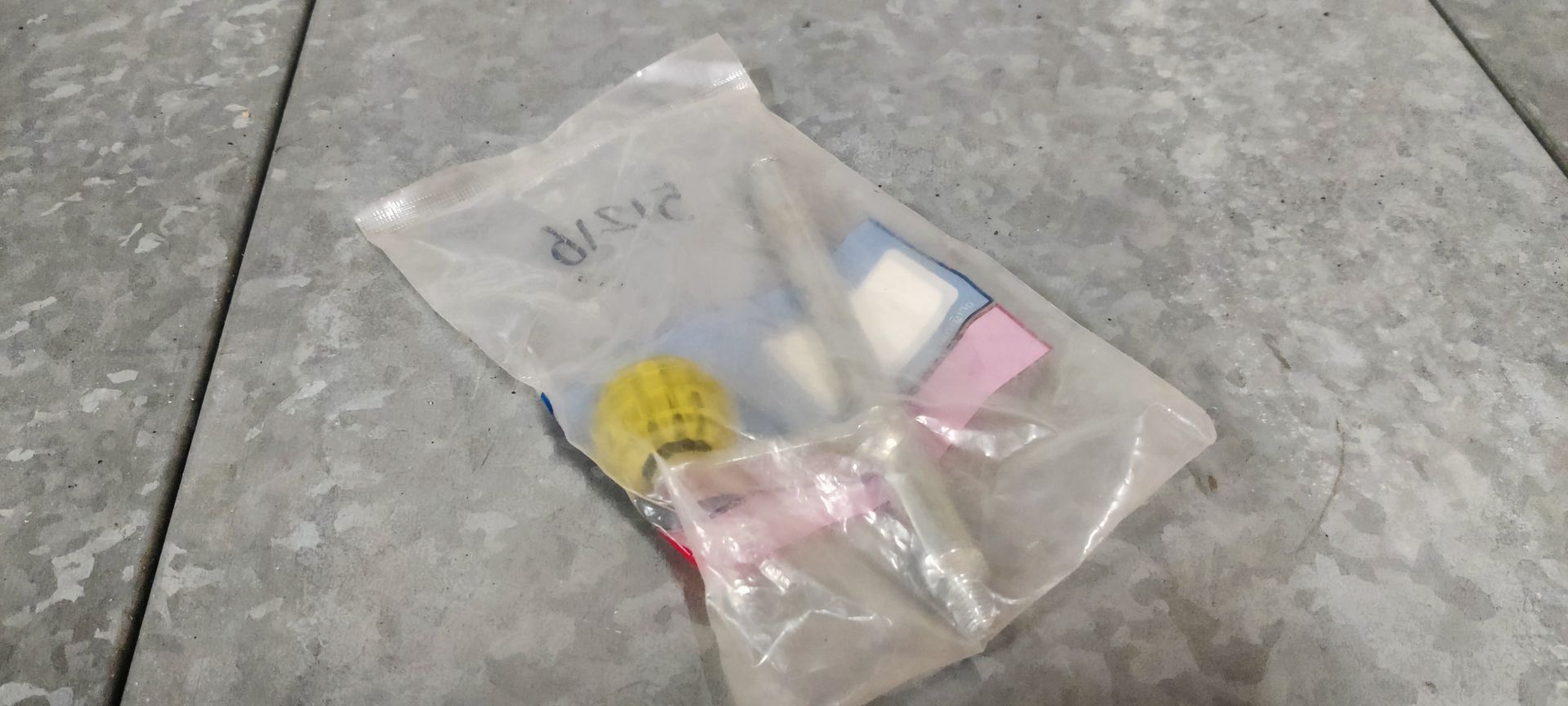 Een plastic zakje met daarin een klein geel kwastje, een witte applicator en roze en blauwe rechthoekige sponsjes.