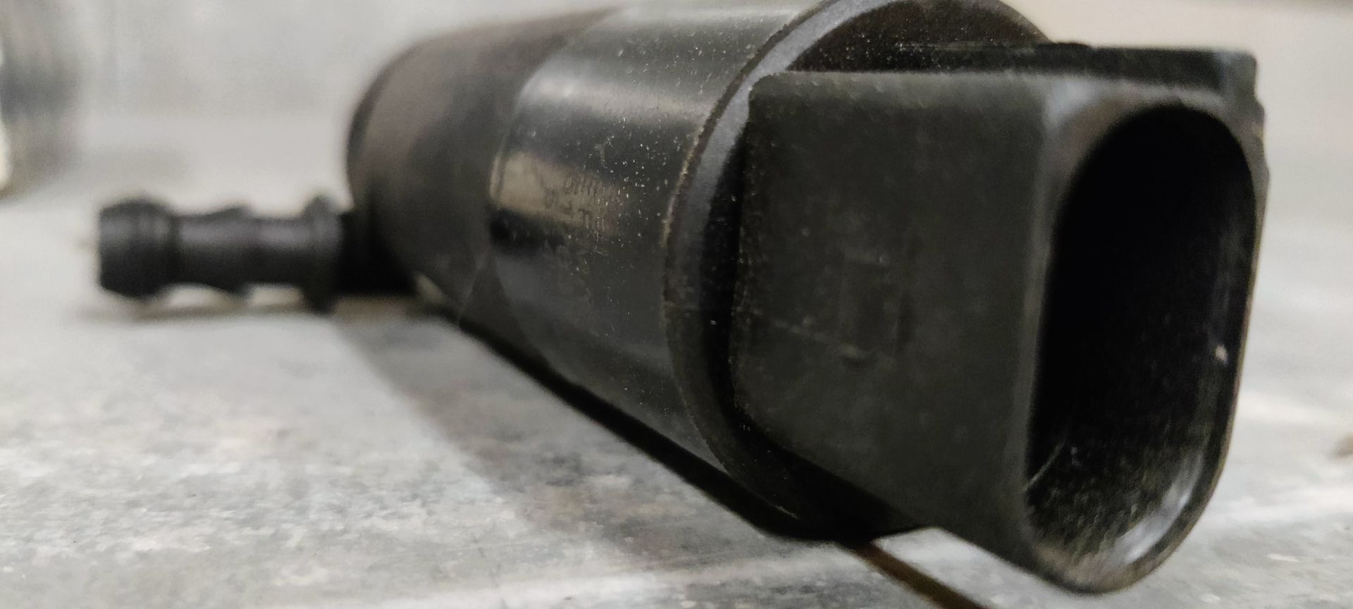 Een zwarte ruitenwisservloeistofpomp voor auto's staat naast de blauw-witte kartonnen verpakking met het merklogo op een grijze vloer.