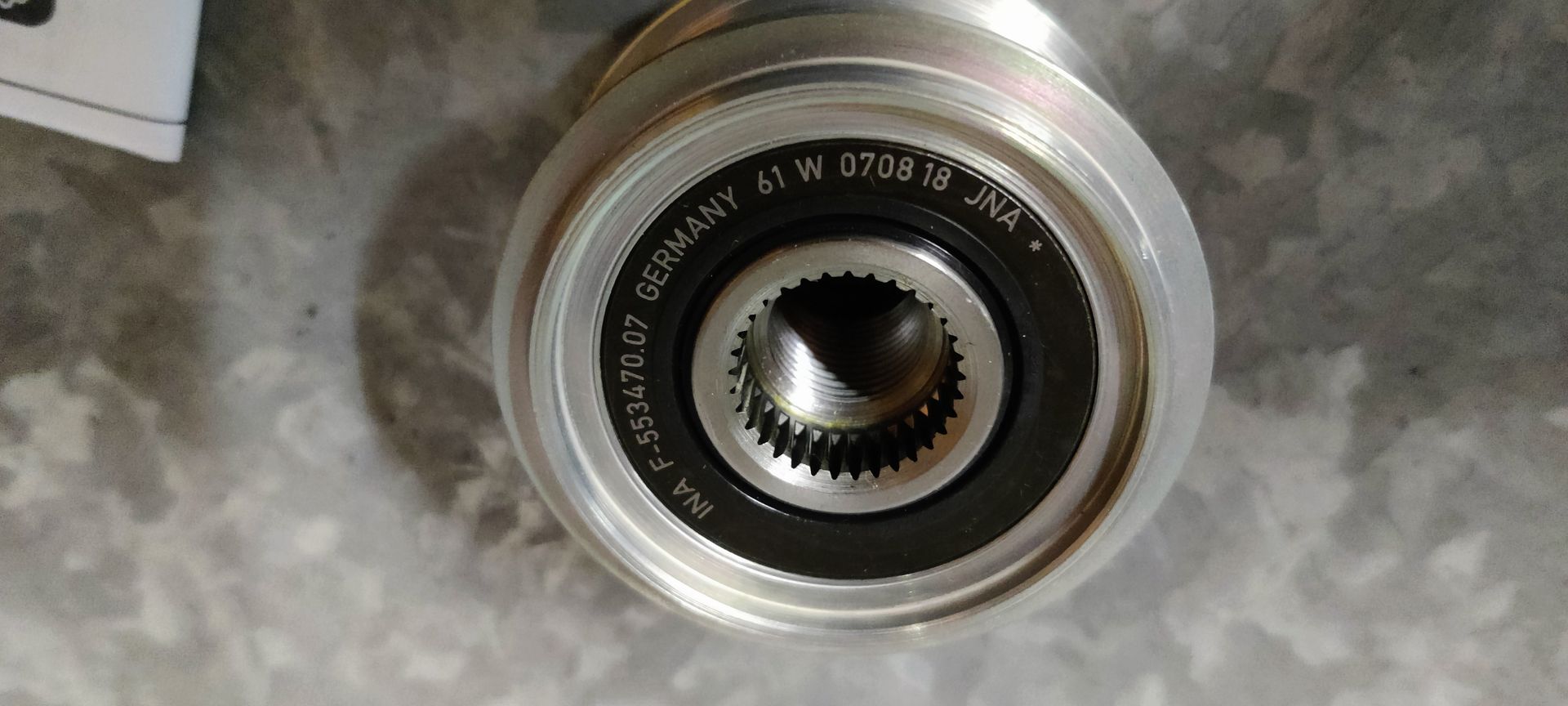 Een Schaeffler OAP-dynamo-poelie in de doos, met beschermkap en handleiding, op een betonnen ondergrond.