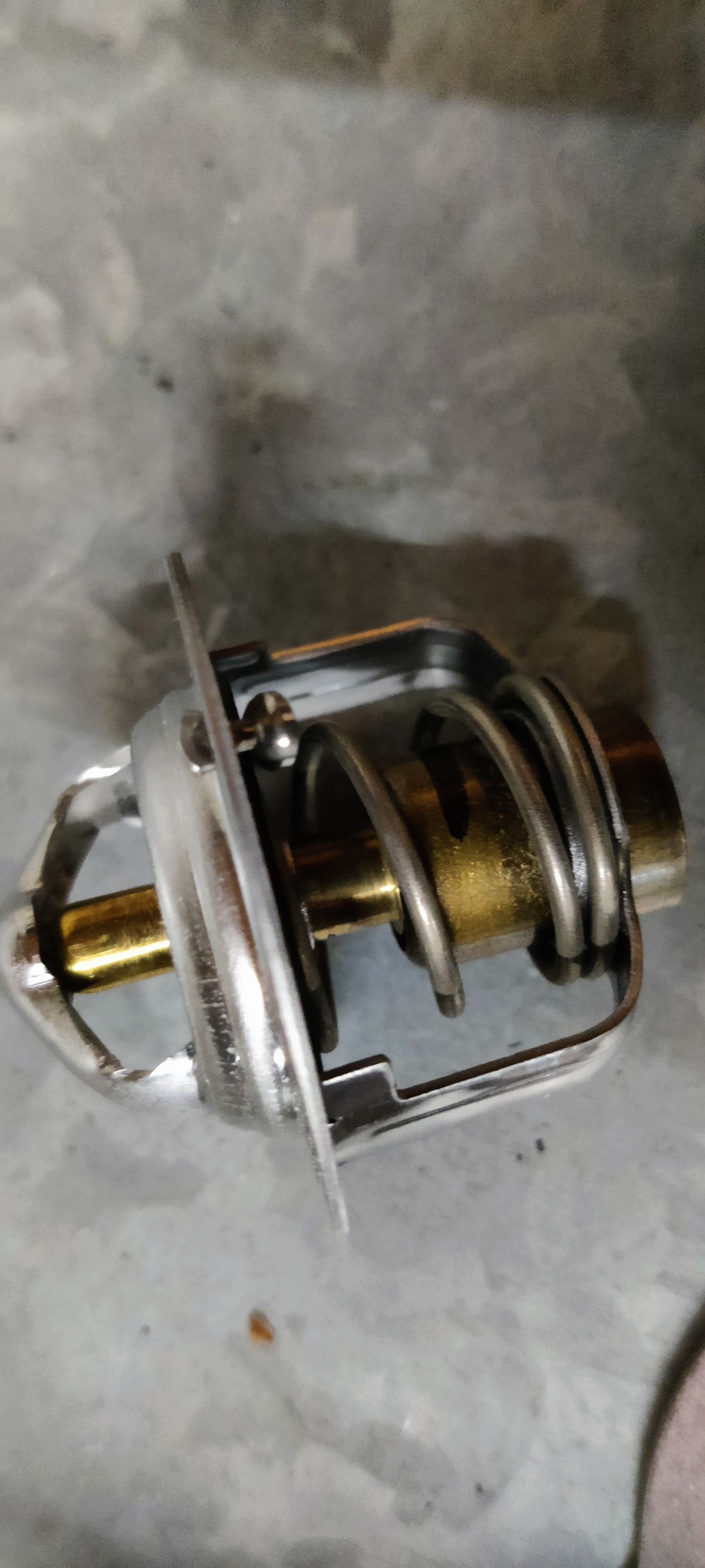 Een thermostaat van het merk Japanparts met bijbehorende papieren pakking, geplaatst op een grijs, gestructureerd oppervlak.