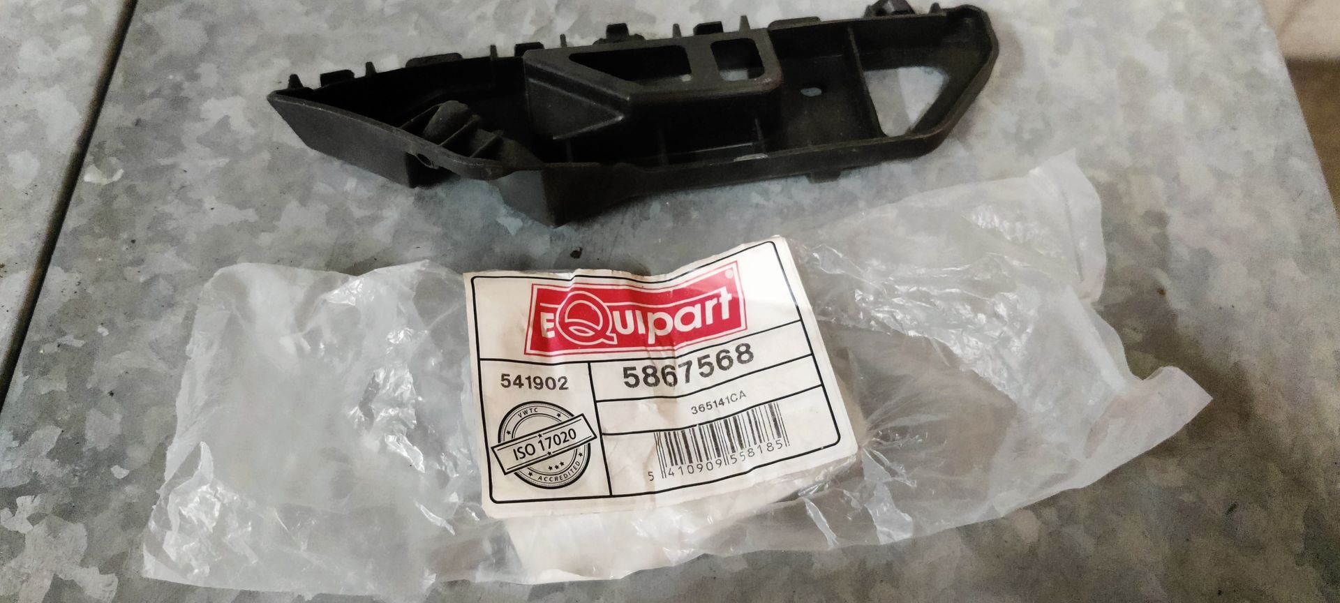 Een zwarte plastic steunbeugel voor een autobumper, met daarachter het witte Niparts-verpakkingslabel op een metalen ondergrond.