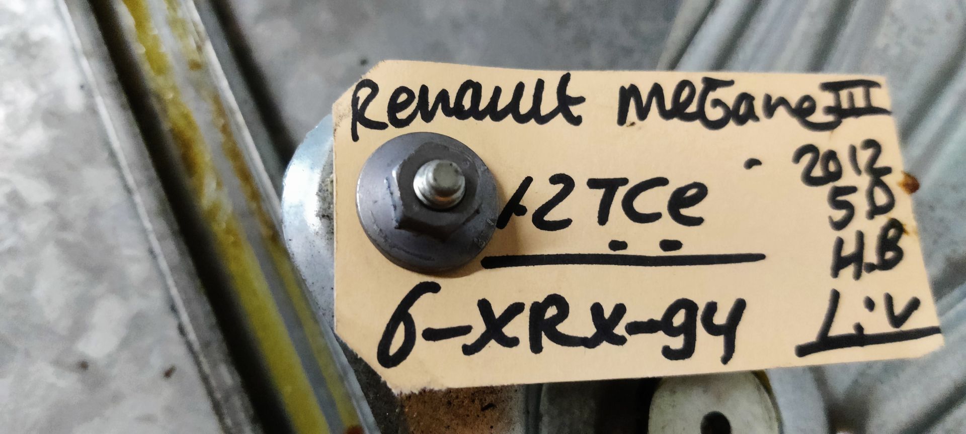 Een metalen raammechanisme voor een elektrische autoruit, met een tandwielmechanisme en een montagerail, op een betonnen vloer.