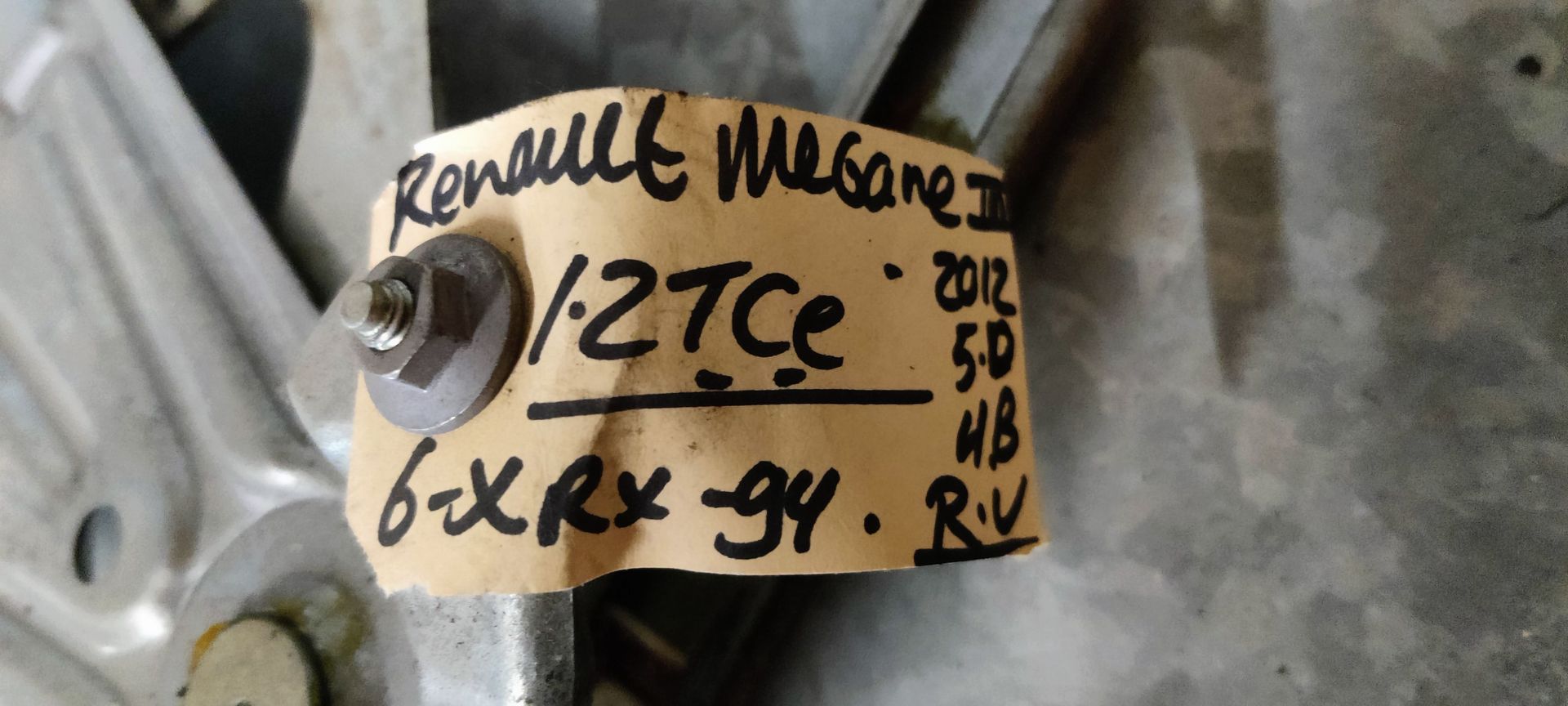 Een metalen raammechanisme van een auto ligt op een grijze tegelvloer.