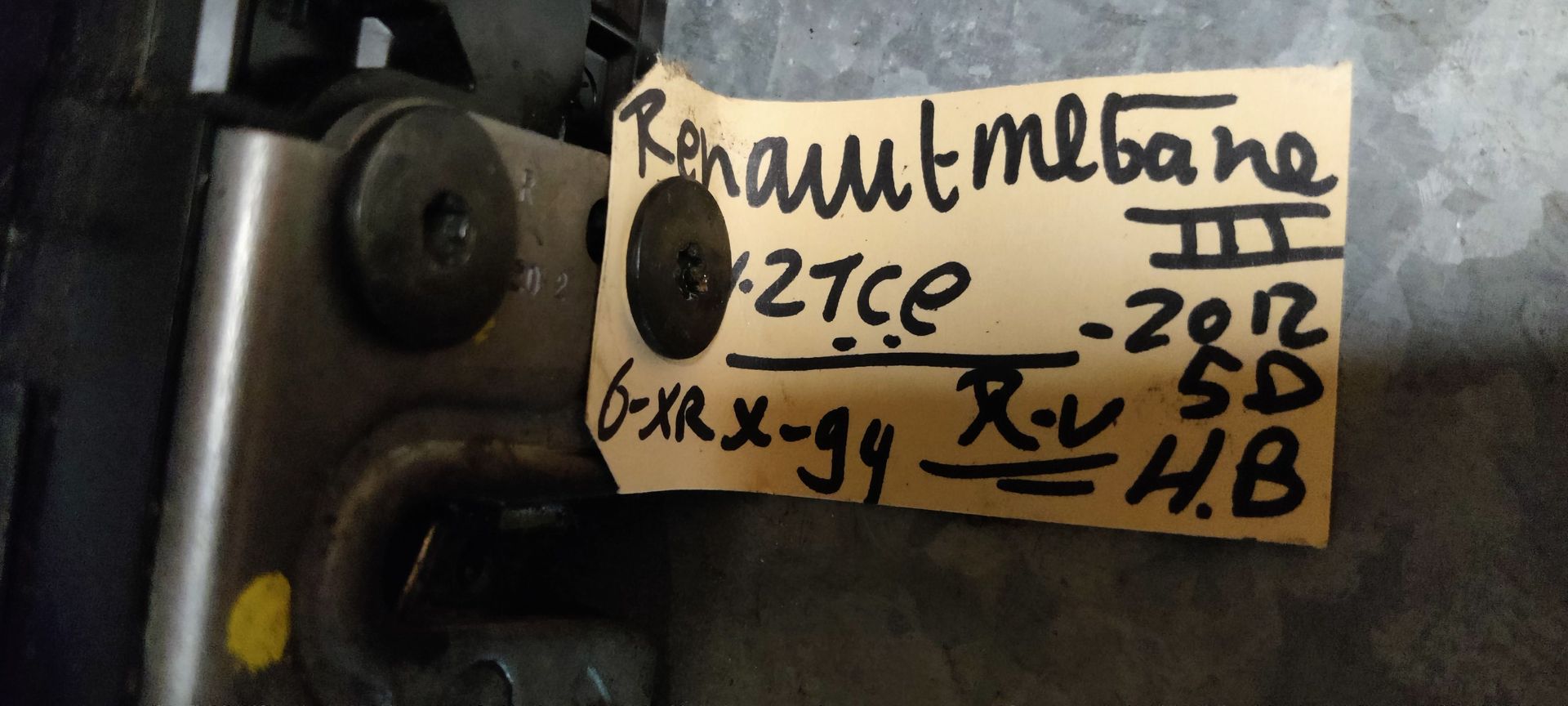 Een zwart autodeurslot met een aangesloten kabel en elektrische connector op een grijze vloer.