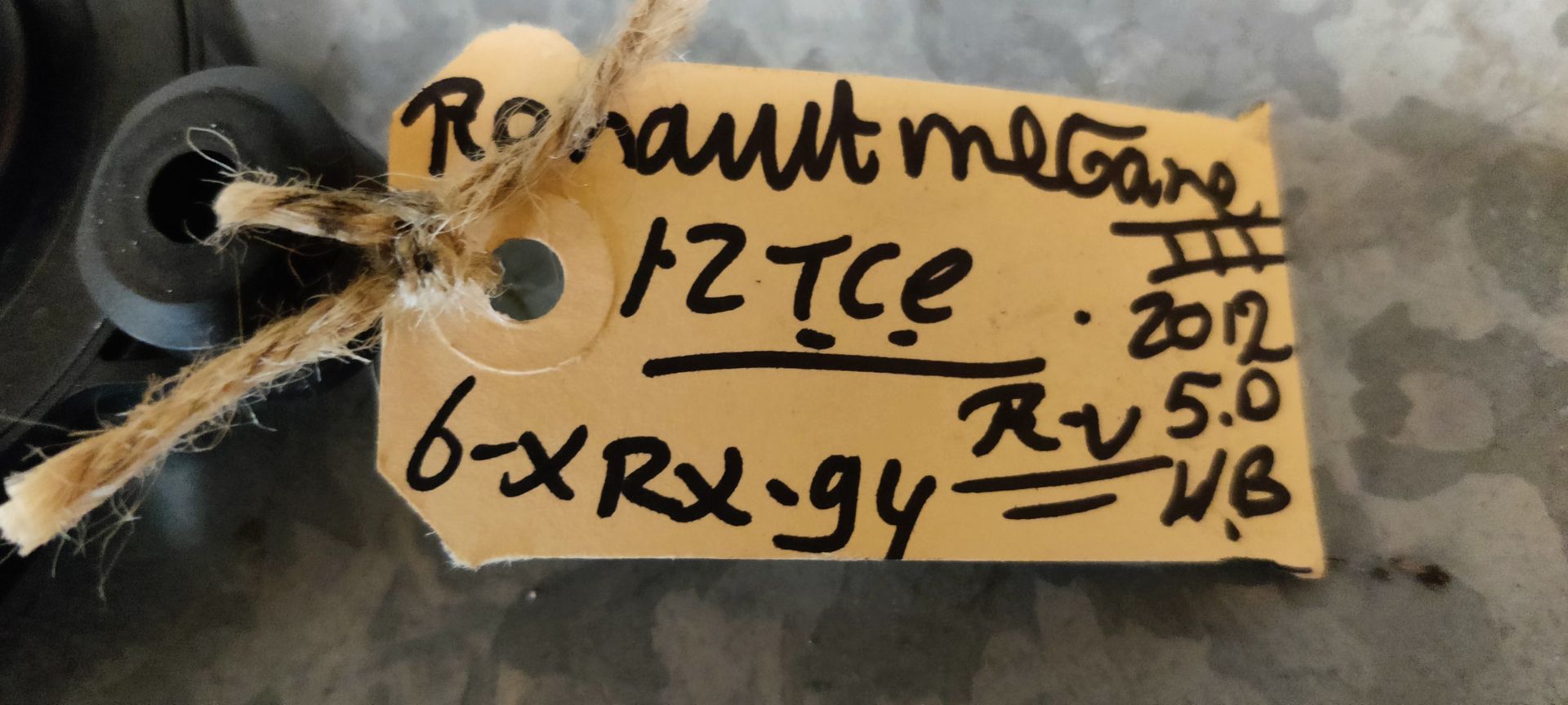 Een zwarte motor voor een elektrisch bedienbaar autoraam met tandwiel, geplaatst op een grijze ondergrond met een handgeschreven identificatielabel.