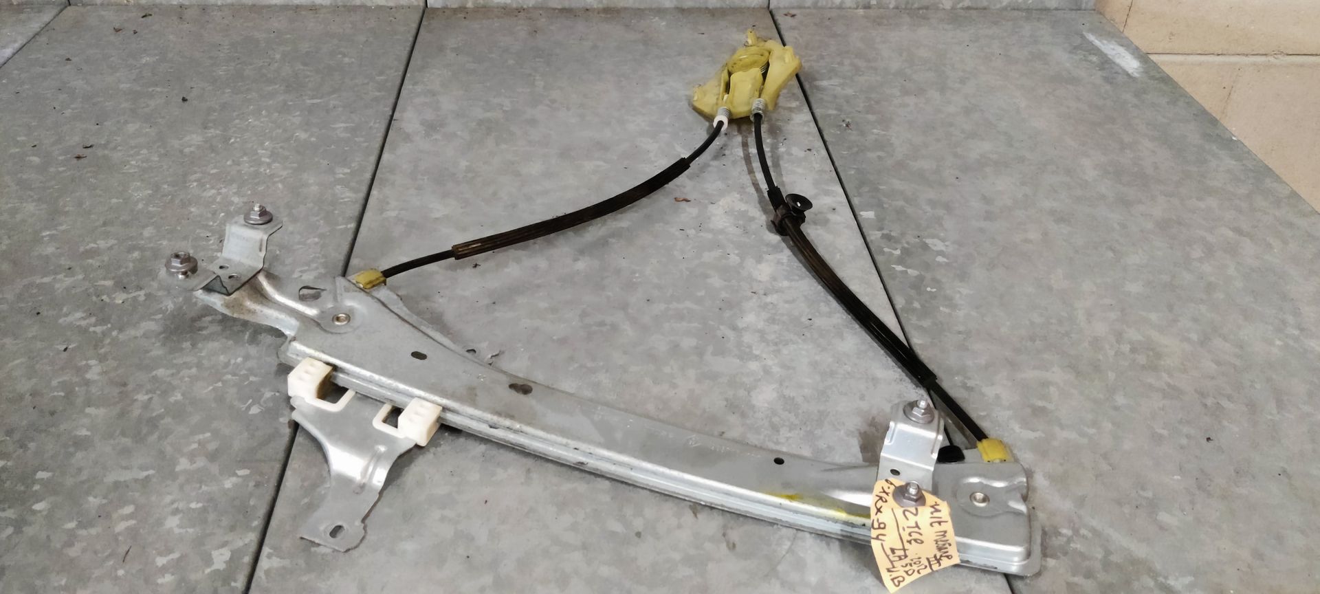 Een metalen raammechanisme voor auto's met zwarte kabels op een grijze ondergrond.