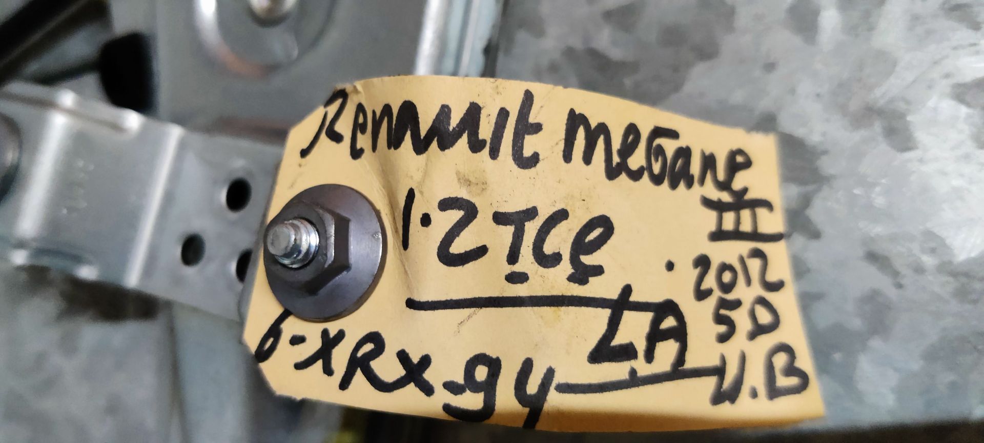 Een metalen raammechanisme voor auto's met zwarte kabels op een grijze ondergrond.