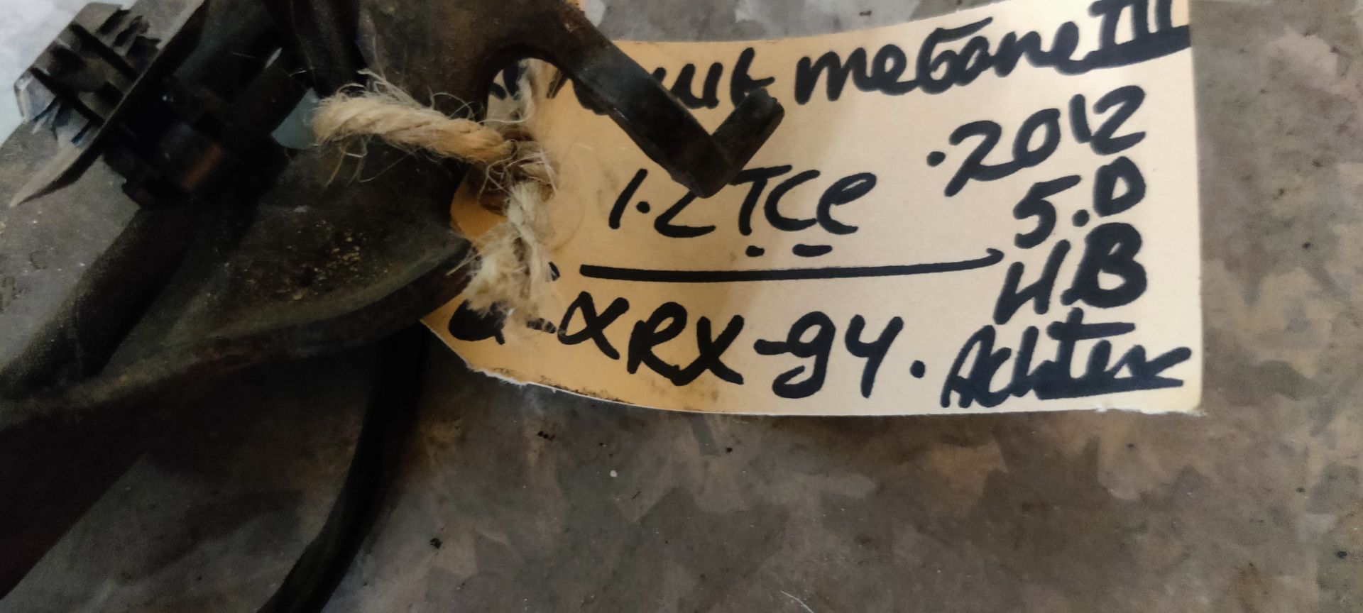 Een zwarte autogordelgesp met een metalen bevestigingsbeugel, rustend op een grijze tegelvloer.