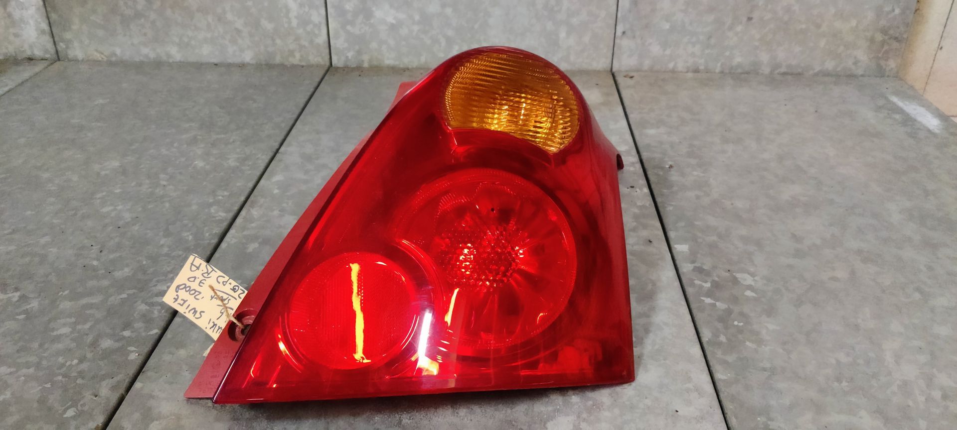 Een driehoekige rode en amberkleurige achterlichtunit met ronde lichtsegmenten, rustend op een grijze tegelondergrond.