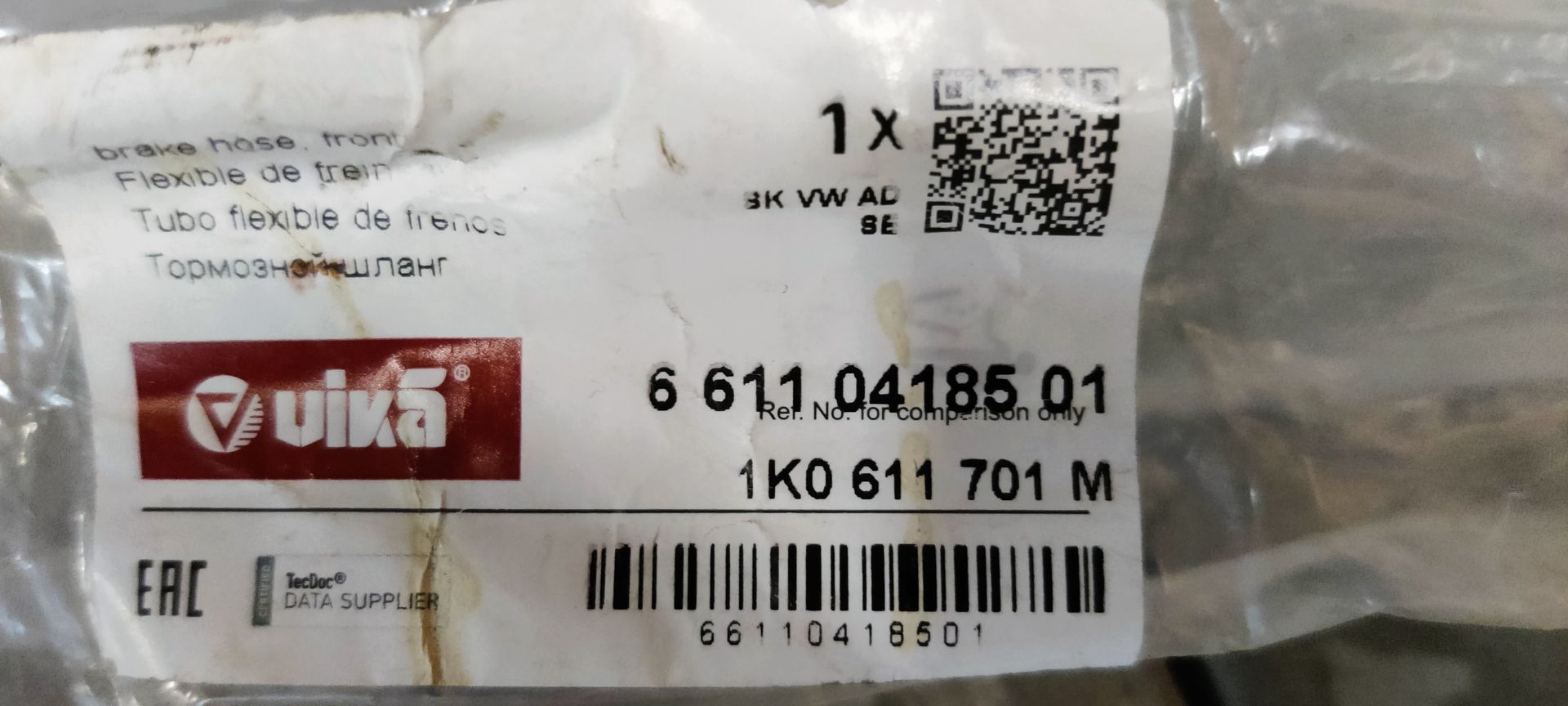 Een zwarte remslang voor auto's met messing schroefdraadaansluitingen, afgebeeld met de originele plastic verpakking.