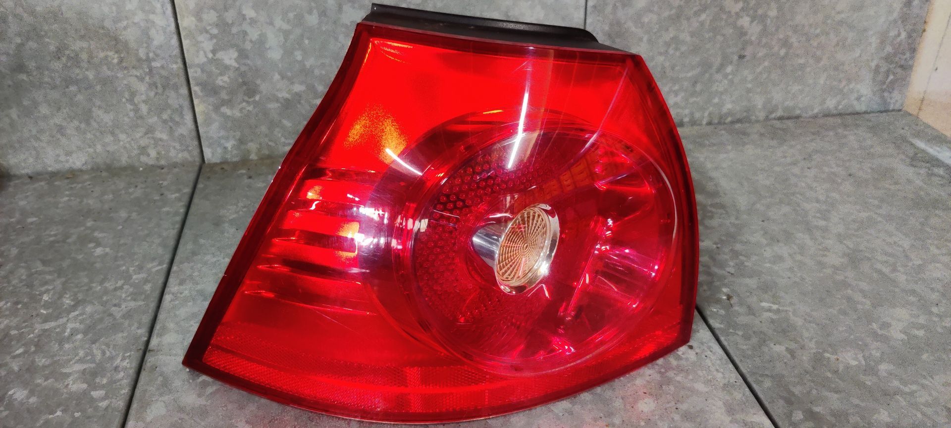 Een rode, driehoekige achterlichtunit voor auto's, met een ronde centrale lens, rustend op een grijs betegeld oppervlak.