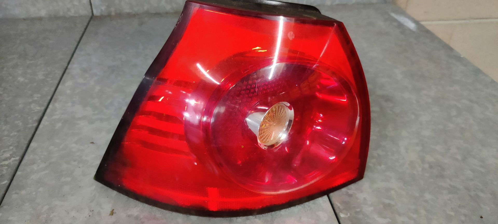 Een rode, driehoekige achterlichtunit voor auto's met een ronde centrale lens, rustend op een grijze ondergrond.