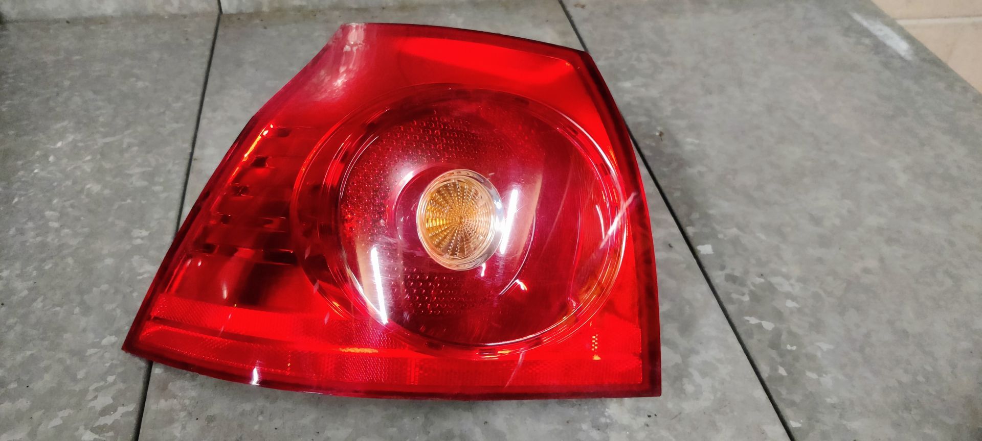 Een rode autoachterlichtunit met een centraal rond knipperlichtlens op een grijze tegelachtergrond.