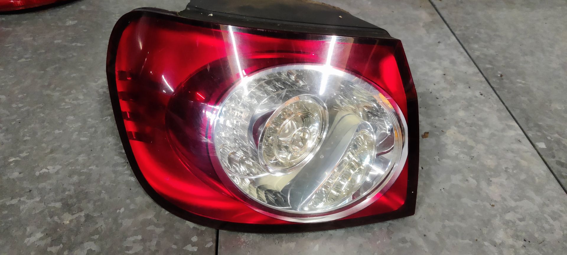 Een rode en transparante achterlichtunit van een auto, rustend op een grijze betonnen ondergrond.