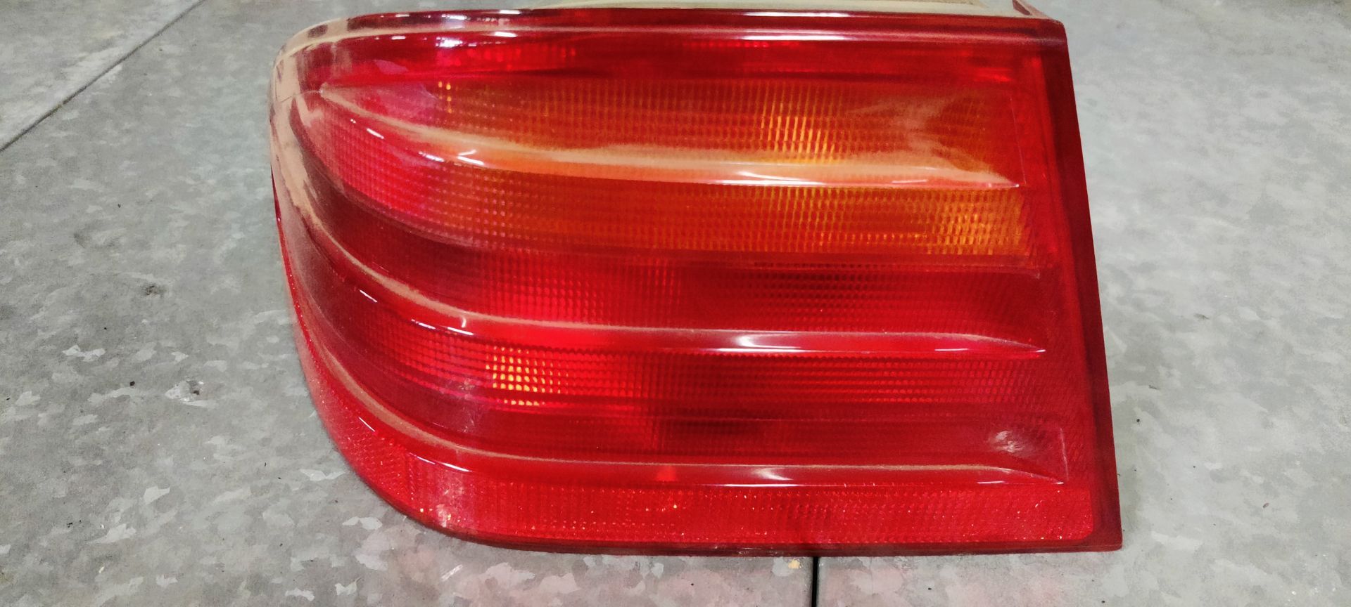 Een rechthoekige achterlichtunit voor een auto met horizontale rode en oranje lichtsecties op een grijs oppervlak.