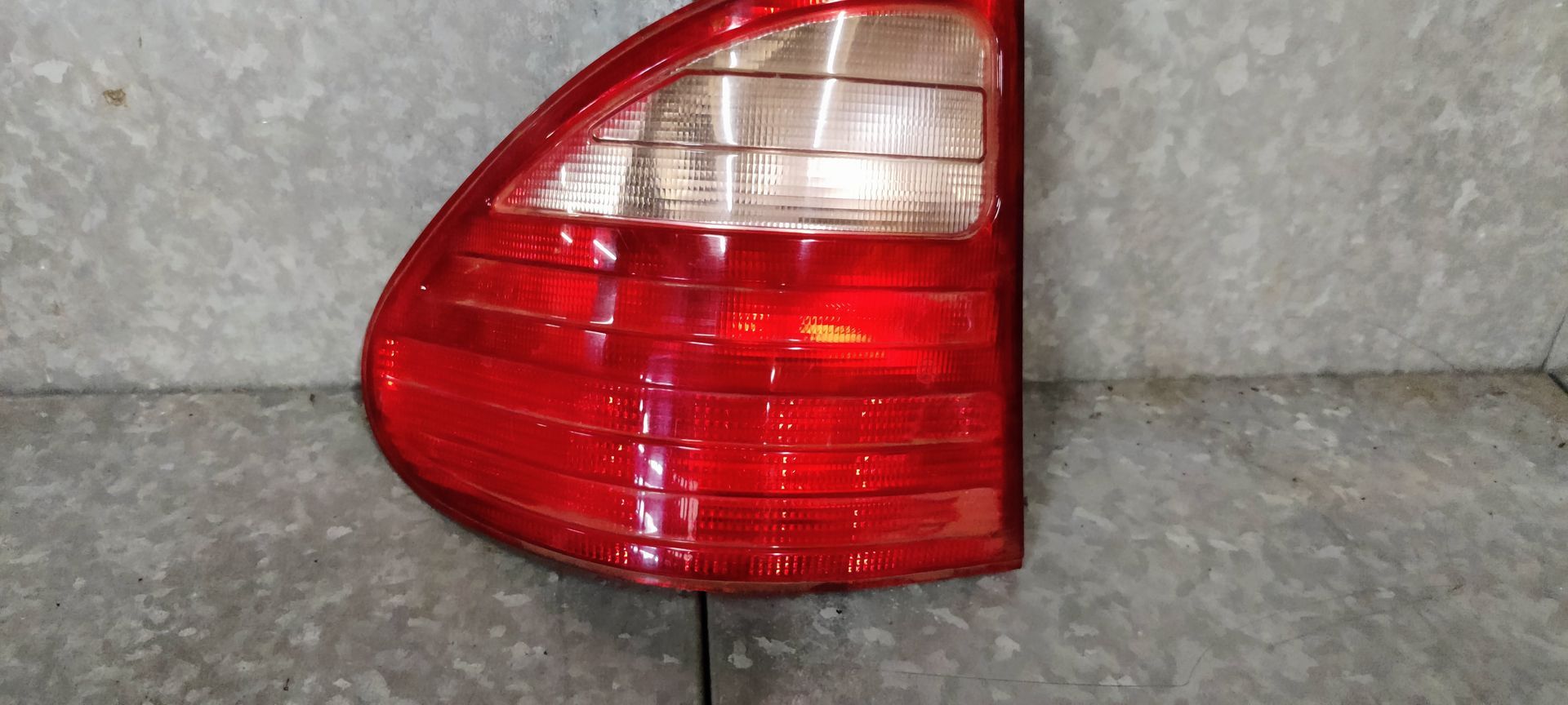 Een rode en transparante achterlichtunit van een auto, van voren gezien tegen een grijze, gestructureerde achtergrond.