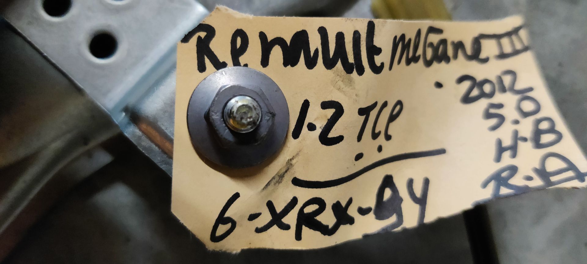 Een raammechanisme voor een auto, met metalen rails, zwarte kabels en een goudkleurige motorbehuizing, op een grijze tegelvloer.