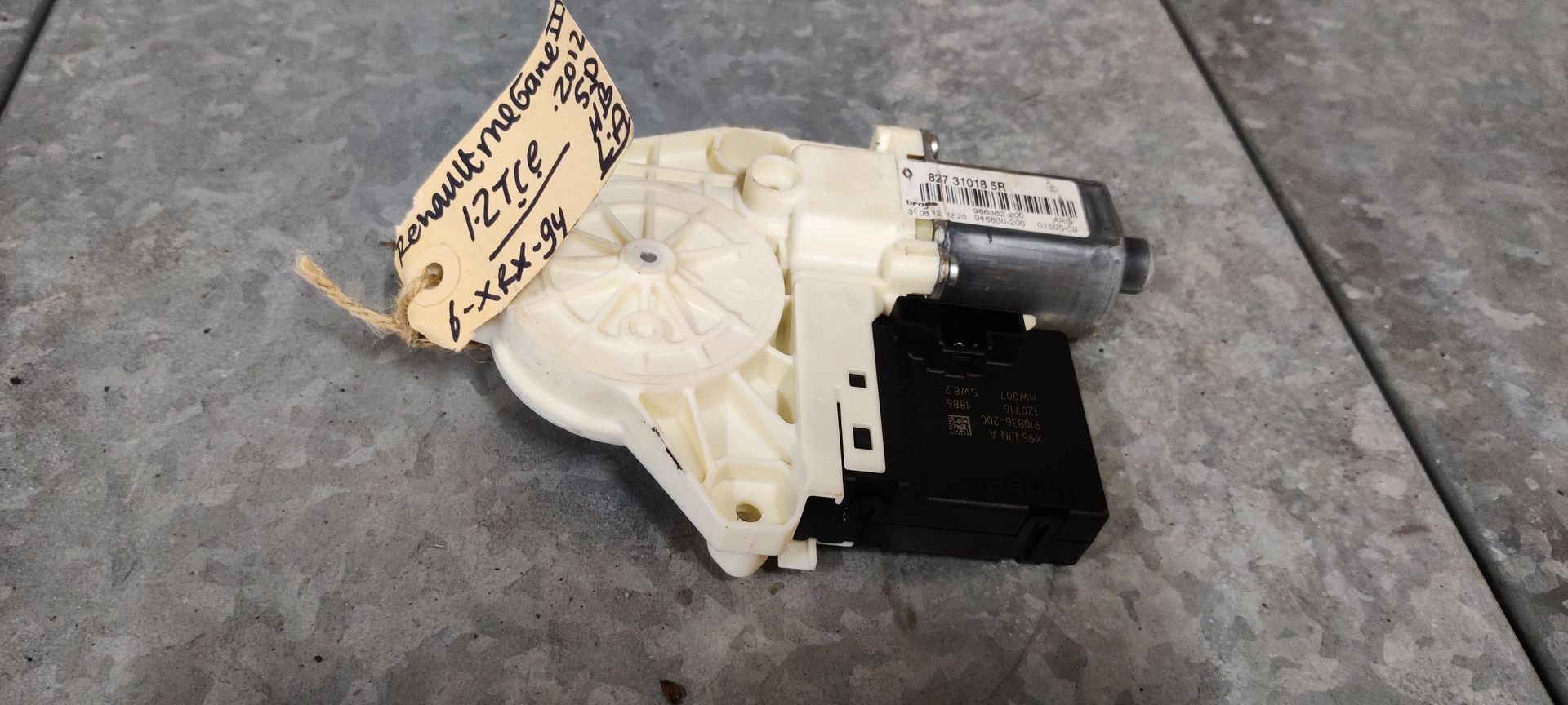 Een wit-zwart plastic raammotor voor auto's met een handgeschreven identificatielabel.