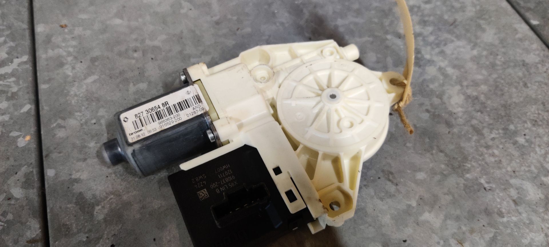 Een wit-grijze raammechanisme-motor voor auto's met een zwarte elektronische regelmodule eraan bevestigd.