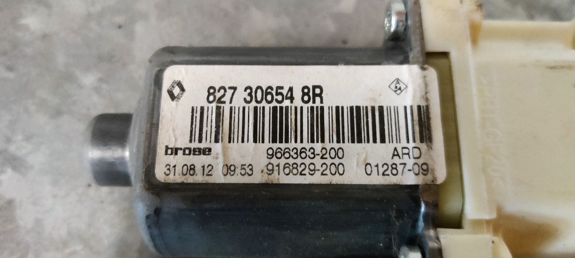 Een wit-grijze raammechanisme-motor voor auto's met een zwarte elektronische regelmodule eraan bevestigd.