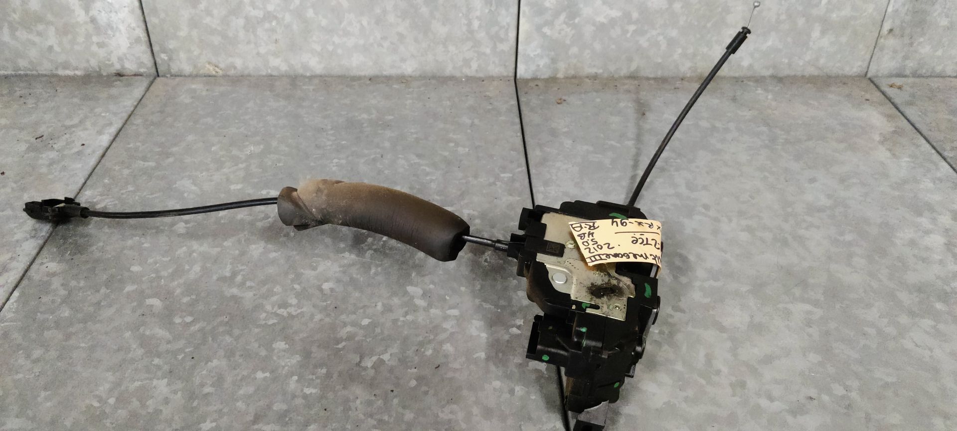 Een actuatormechanisme voor een autodeurslot met aangesloten kabels, afgebeeld tegen een grijze, gestructureerde achtergrond.