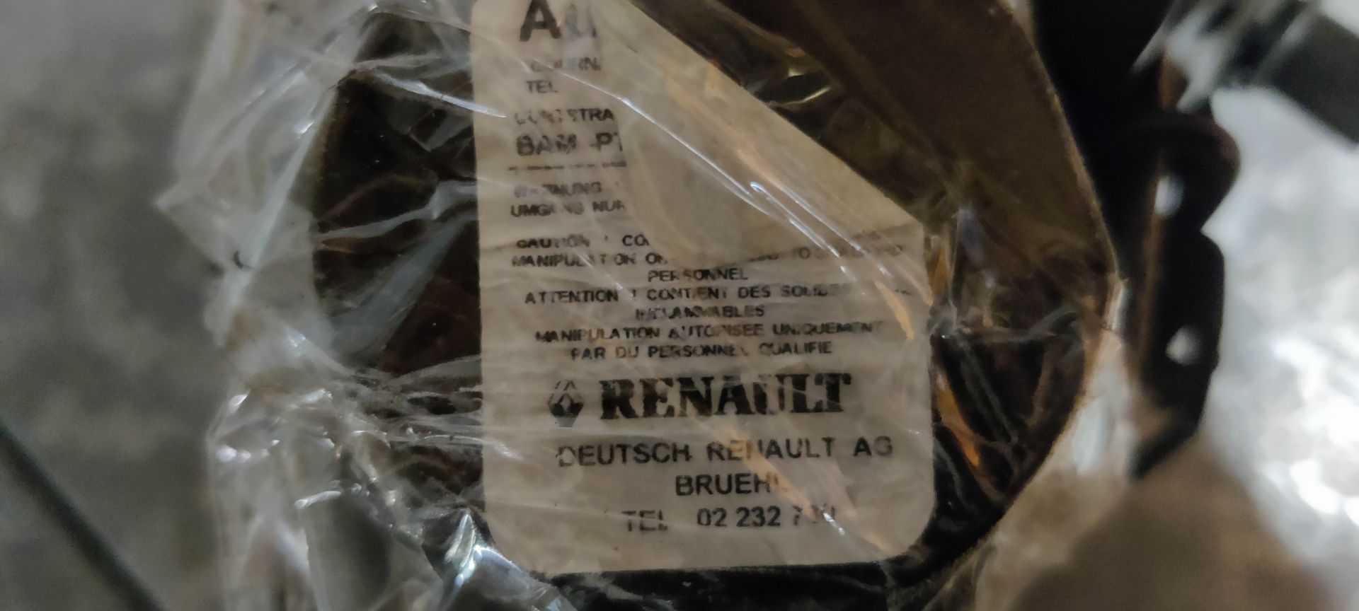 Een wit oprolmechanisme voor autogordels met een geel label, rustend op een grijze betonnen ondergrond.