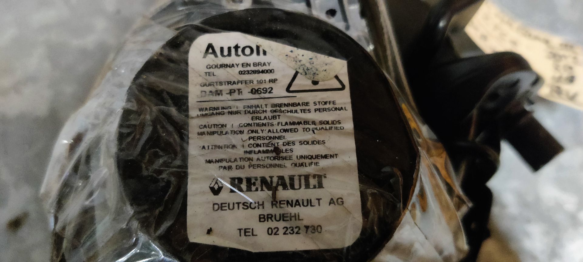 Een oprolmechanisme voor een autogordel, inclusief de gordelband en een identificatielabel, op een grijze ondergrond.