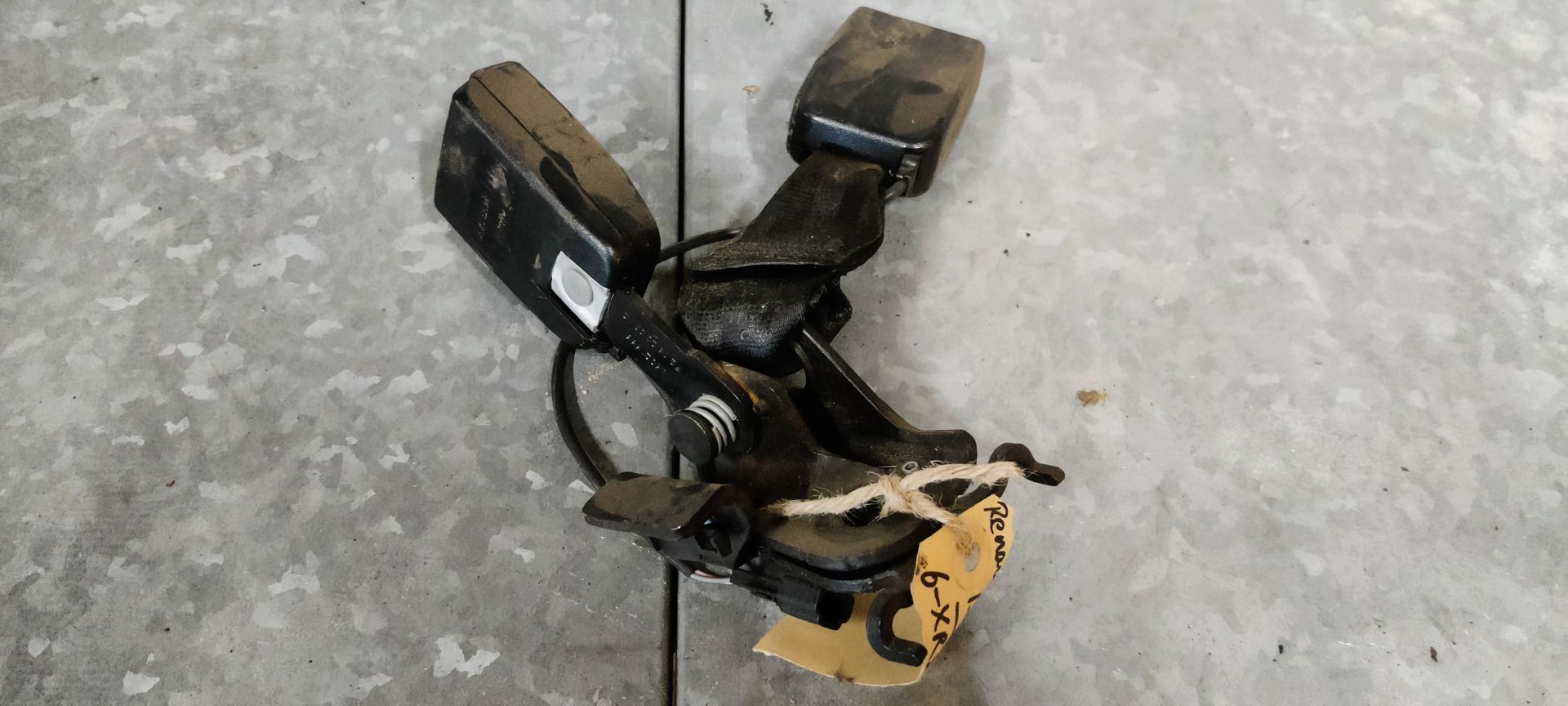 Twee zwarte bevestigingspunten voor autogordels, gemonteerd op een metalen beugel op een grijze betonnen vloer.