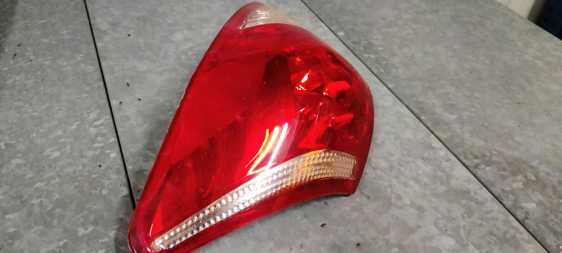 Een rode autoachterlichtunit met een transparant knipperlichtgedeelte, van bovenaf gefotografeerd op een grijze achtergrond.