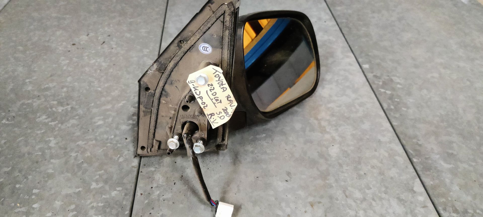 Een autospiegel met aangesloten kabelboom, rustend op een betonnen ondergrond met een handgeschreven label eraan.