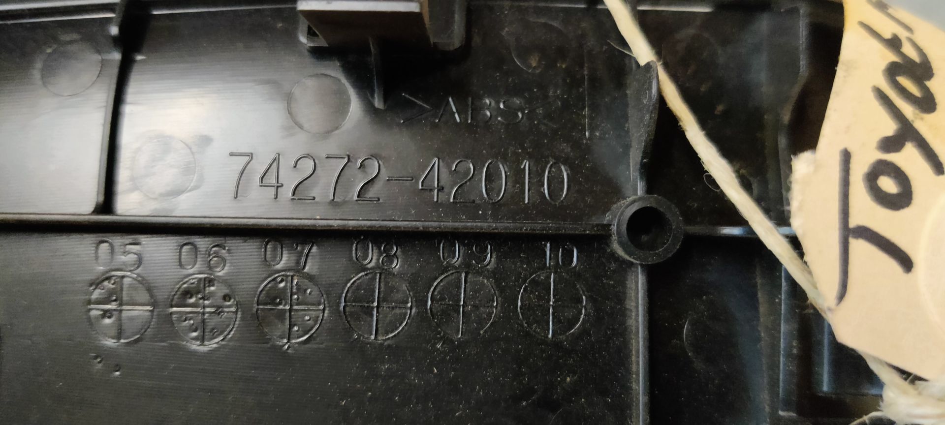 Een zwarte autodeurhendel met een aangehecht identificatielabel, rustend op een grijze betonnen ondergrond.