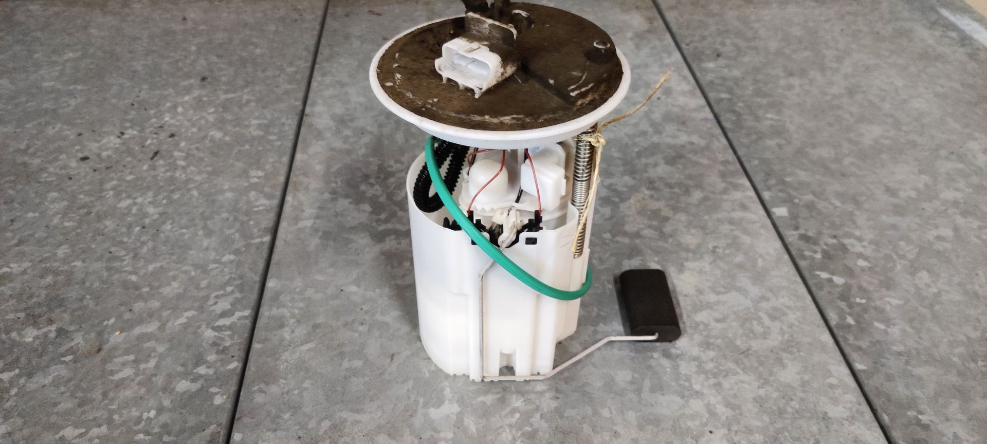 Alfa Romeo MiTo tankvlotter. gebruikte brandstofpompunit met een witte plastic behuizing en een vlotter voor de brandstofniveausensor, op een grijze vloer.