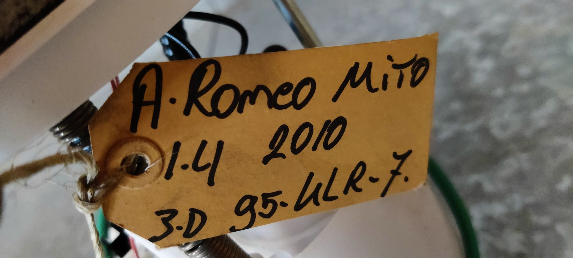 Alfa Romeo MiTo tankvlotter. gebruikte brandstofpompunit met een witte plastic behuizing en een vlotter voor de brandstofniveausensor, op een grijze vloer.