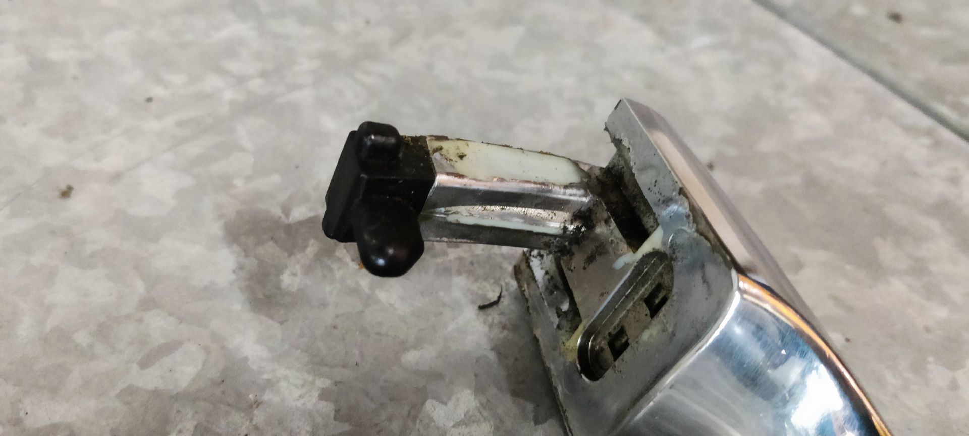 Alfa Romeo MiTo deurklink links. Een verchroomde autodeurhendel met een ingebouwd slotcilindermechanisme, rustend op een grijze tegelondergrond.