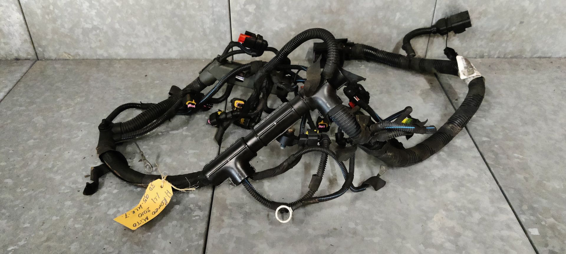 Alfa Romeo MiTo kabelboom naar de motor. Een zwarte autokabelboom met meerdere connectoren en een geel identificatielabel op een tegelvloer.