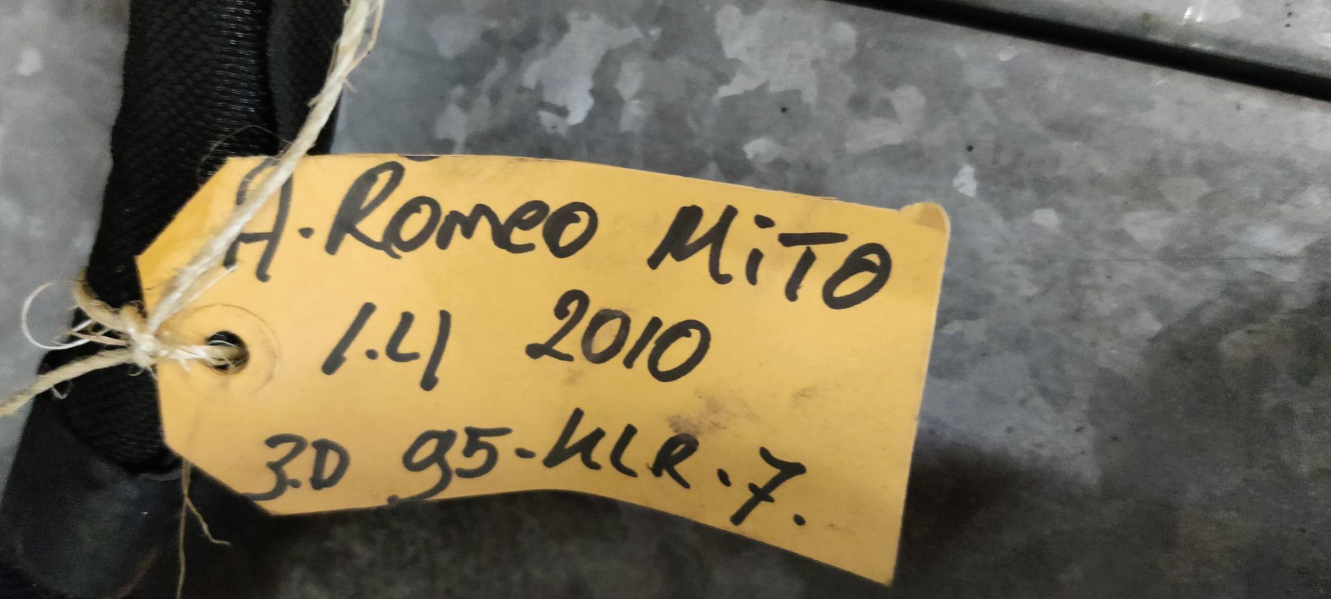 Alfa Romeo MiTo kabelboom naar de motor. Een zwarte autokabelboom met meerdere connectoren en een geel identificatielabel op een tegelvloer.