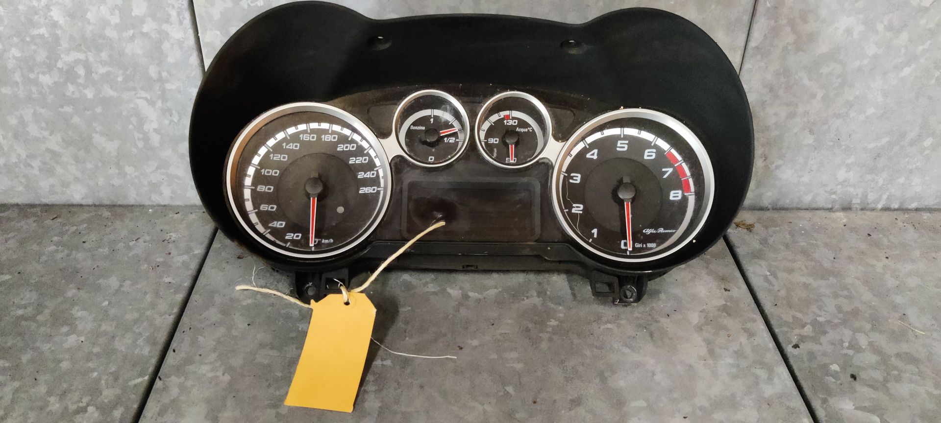 Alfa Romeo MiTo dashboard. Een zwart instrumentenpaneel voor auto's met een snelheidsmeter, toerenteller en twee kleinere meters met een geel label.