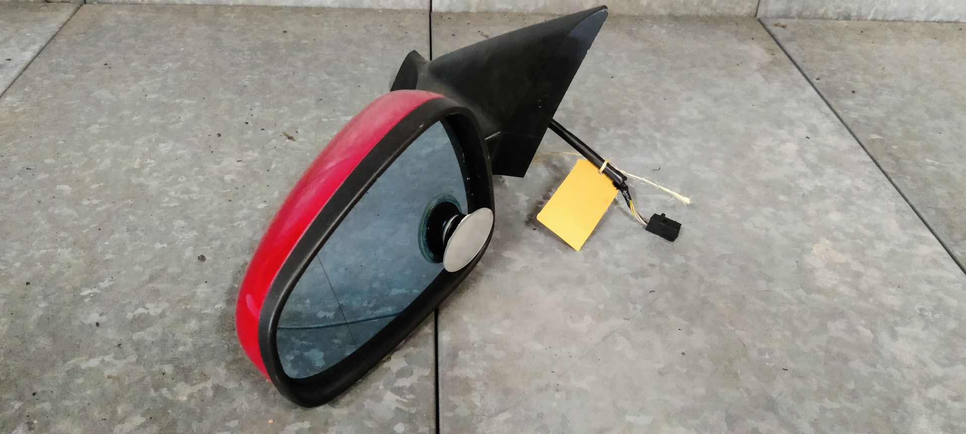 Een rode autospiegel met een zwarte montagebeugel, kabelboom en een geel identificatielabel.