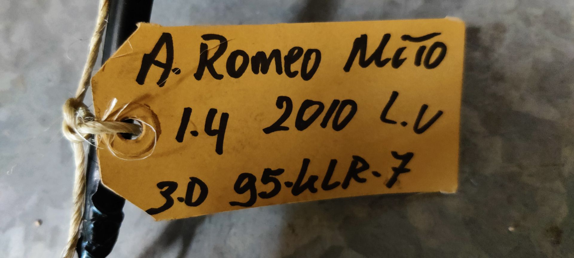 Een rode autospiegel met een zwarte montagebeugel, kabelboom en een geel identificatielabel.