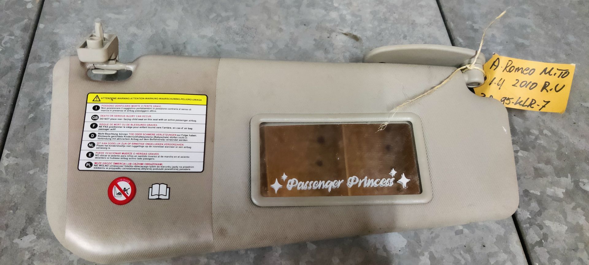 Alfa Romeo MiTo, een beige zonneklep voor in de auto met een waarschuwingslabel, een make-upspiegel met een sticker